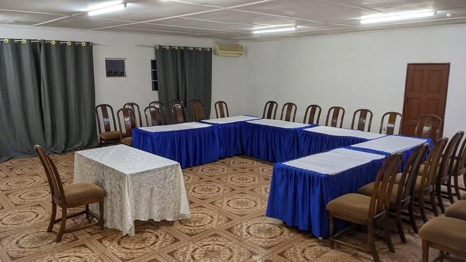 Conference hall with blue-draped tables in a U shape, wooden chairs and grey curtains