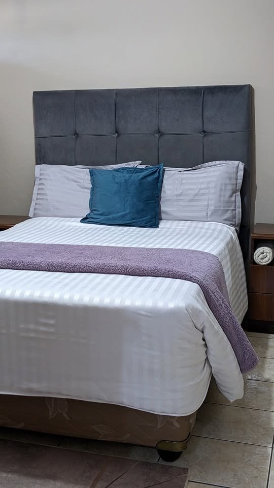 Double bed with a grey padded headboard, white striped linen, a teal cushion and a purple throw